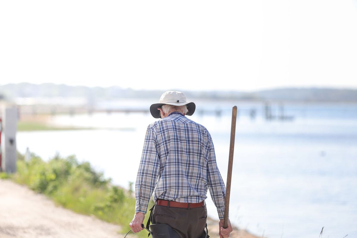 An older man in a sun hat walking along the riverbank
