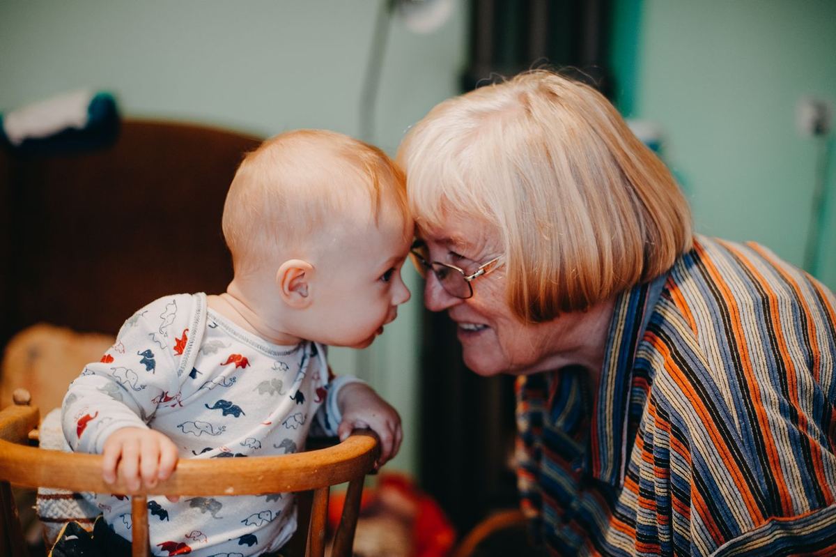 A grandmother touching foreheads with her laughing baby grandchild